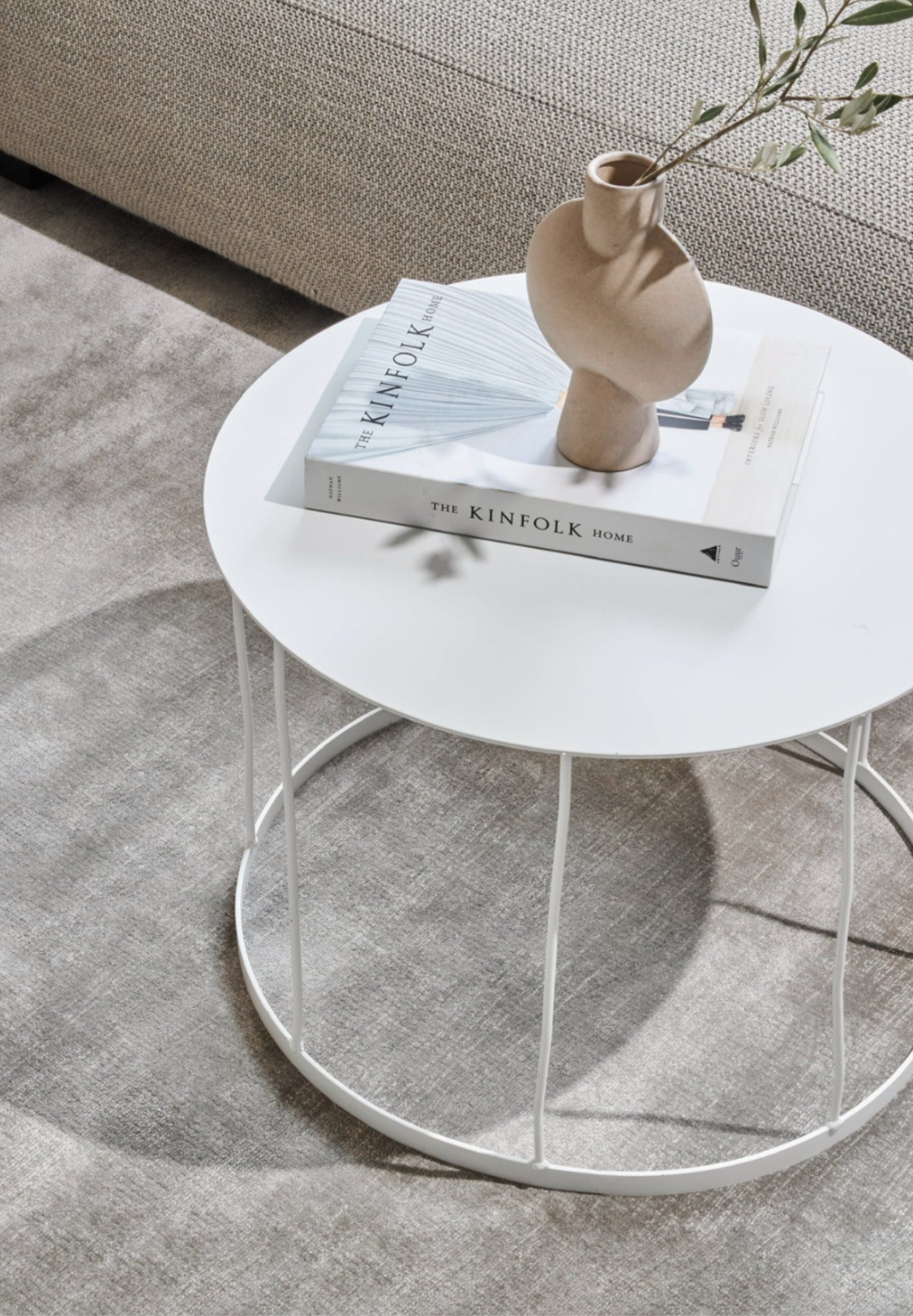 Round white coffee table with a vase and books on a gray carpet