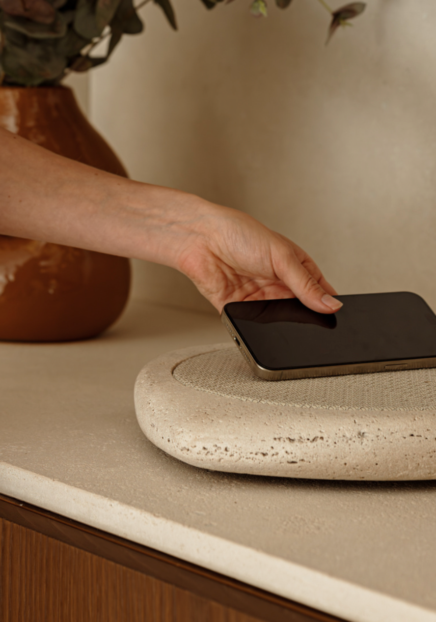 Person placing a smartphone on a wireless charging pad with a vase in the background