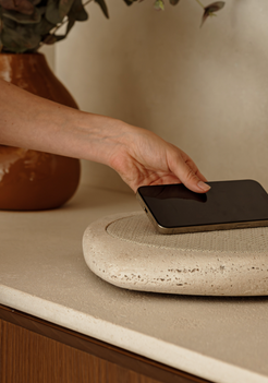 Person placing a smartphone on a wireless charging pad with a vase in the background